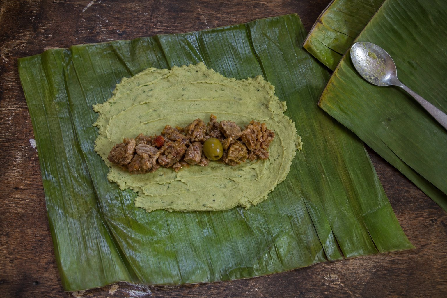 Green banana and root-vegetable masa spread on banana leaf with pork filling for pasteles.