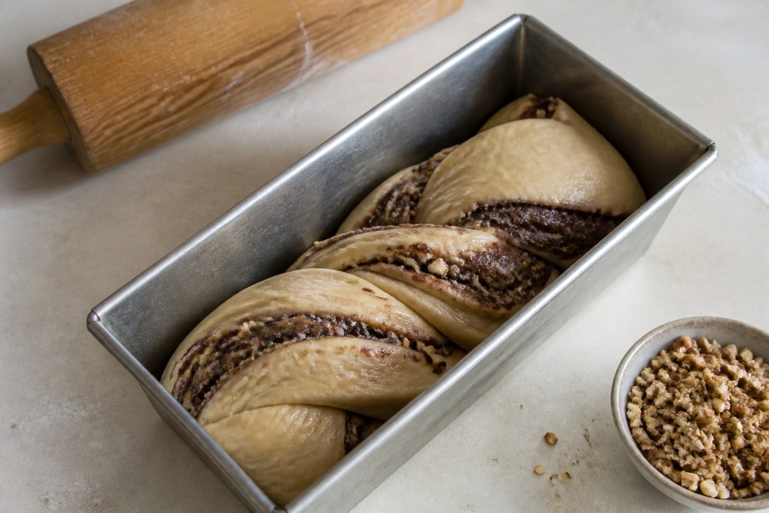 Twisted walnut-cocoa cozonac dough resting in a metal loaf pan before proofing.