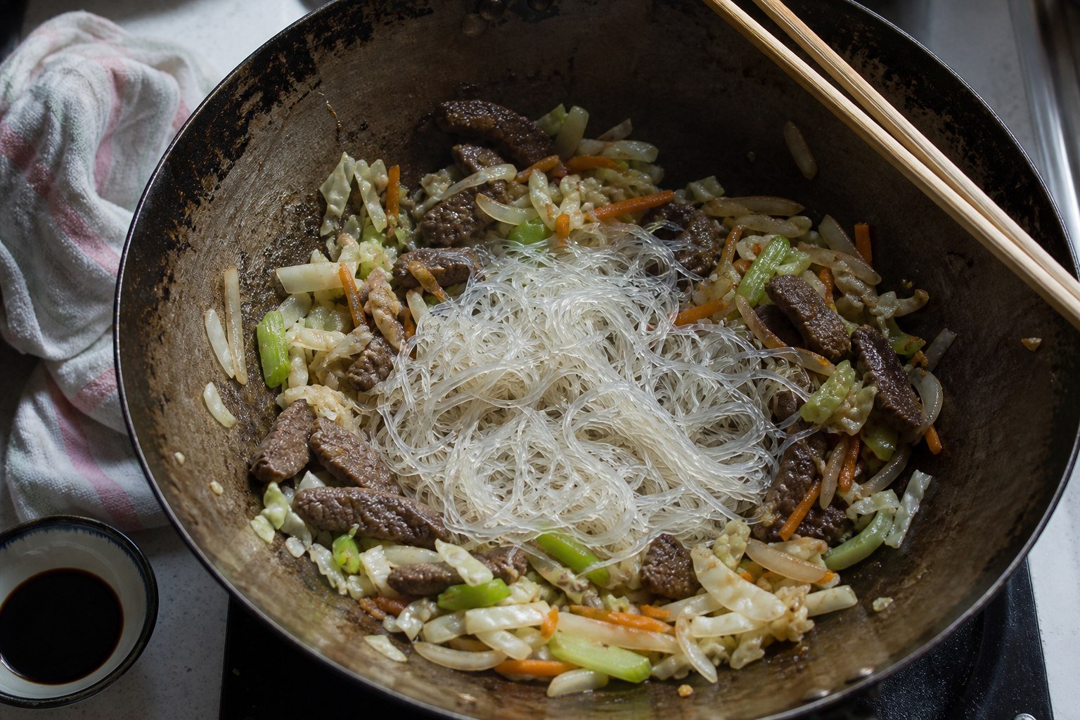 Soaked glass noodles added to a wok of beef and vegetables while making Samoan sapasui.