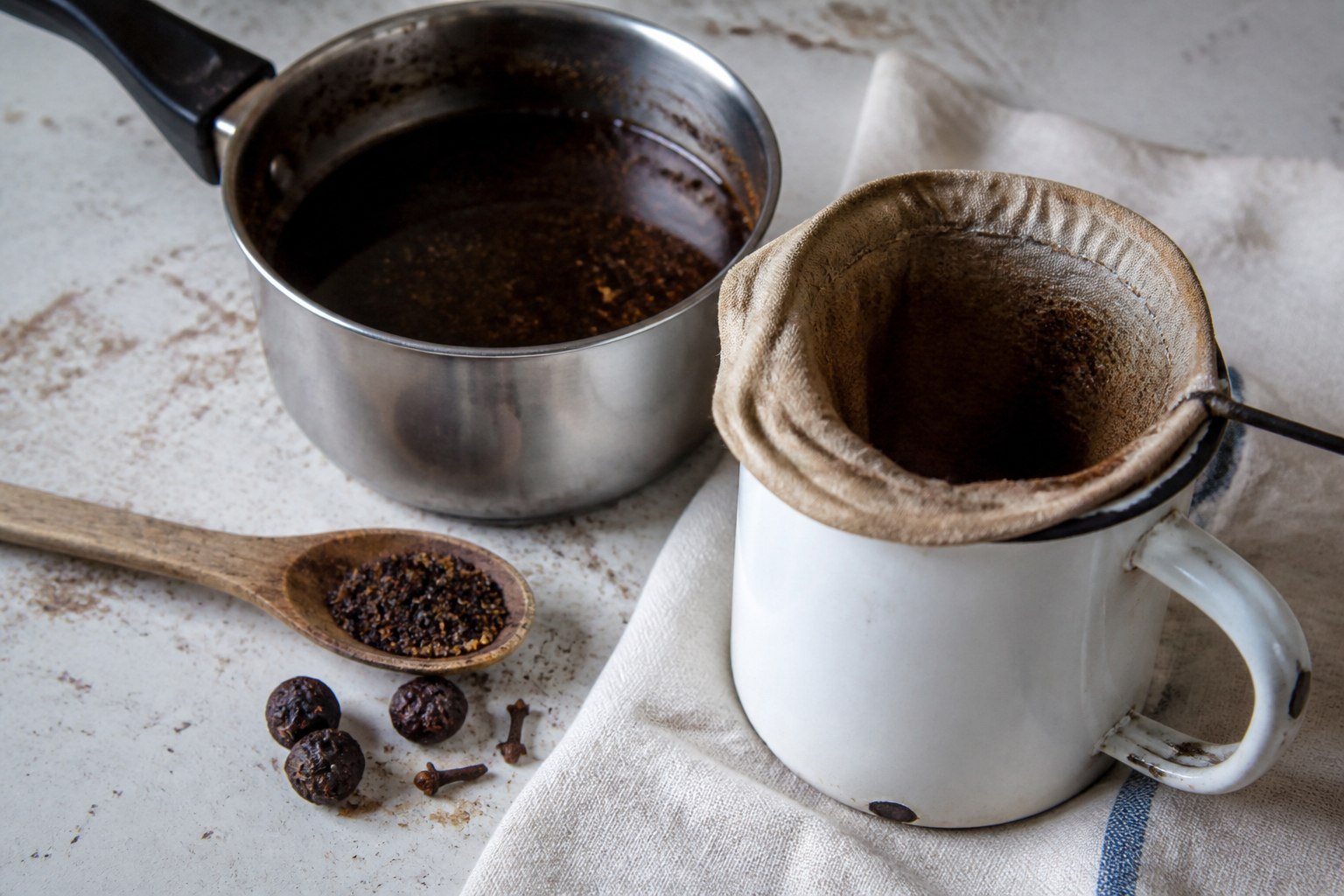 Cafe Touba coffee and spices beside a cloth filter and enamel jug.