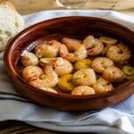 Spanish gambas al ajillo with shrimp, sliced garlic, chile, olive oil, and bread.