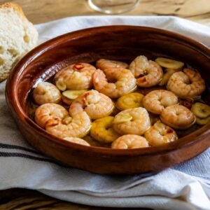 Spanish gambas al ajillo with shrimp, sliced garlic, chile, olive oil, and bread.