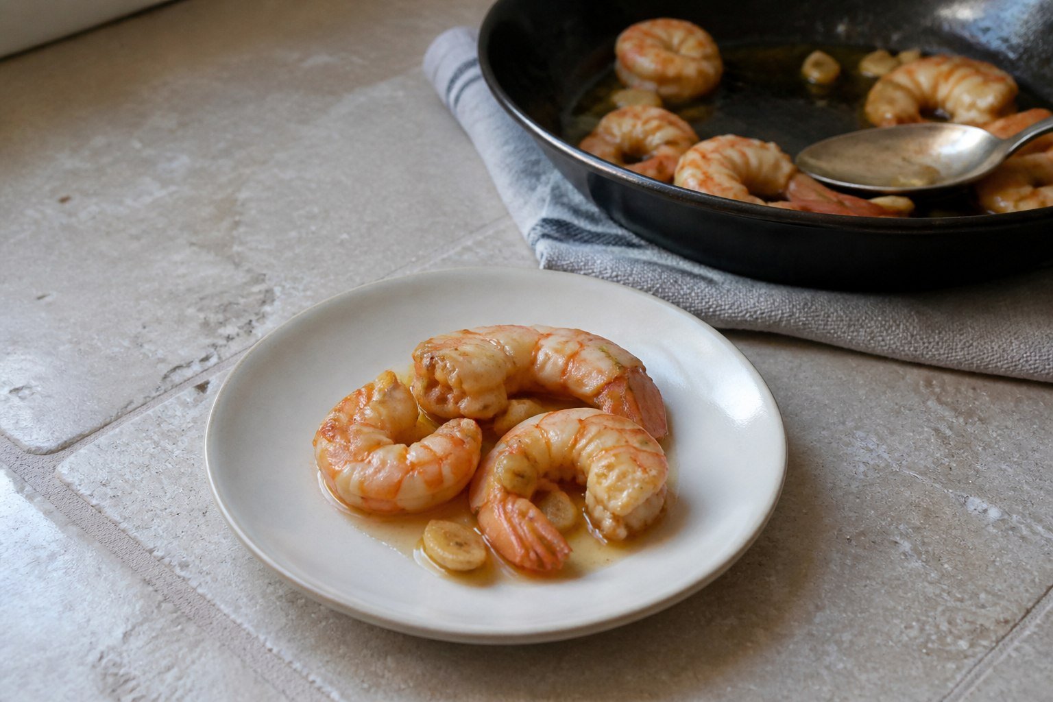 A small serving of gambas al ajillo beside the pan of garlic shrimp.