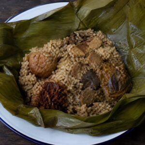 Sri Lankan lamprais opened on banana leaf with stock rice, curry, frikadeller, eggplant, and sambol.