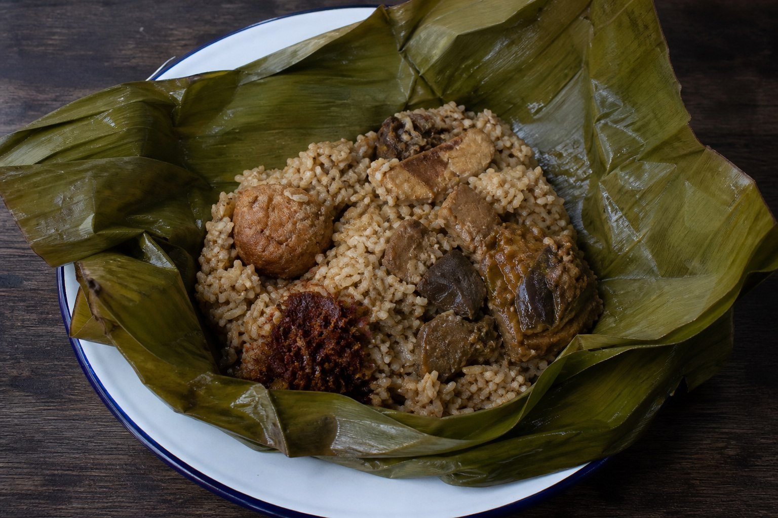 Sri Lankan lamprais opened on banana leaf with stock rice, curry, frikadeller, eggplant, and sambol.