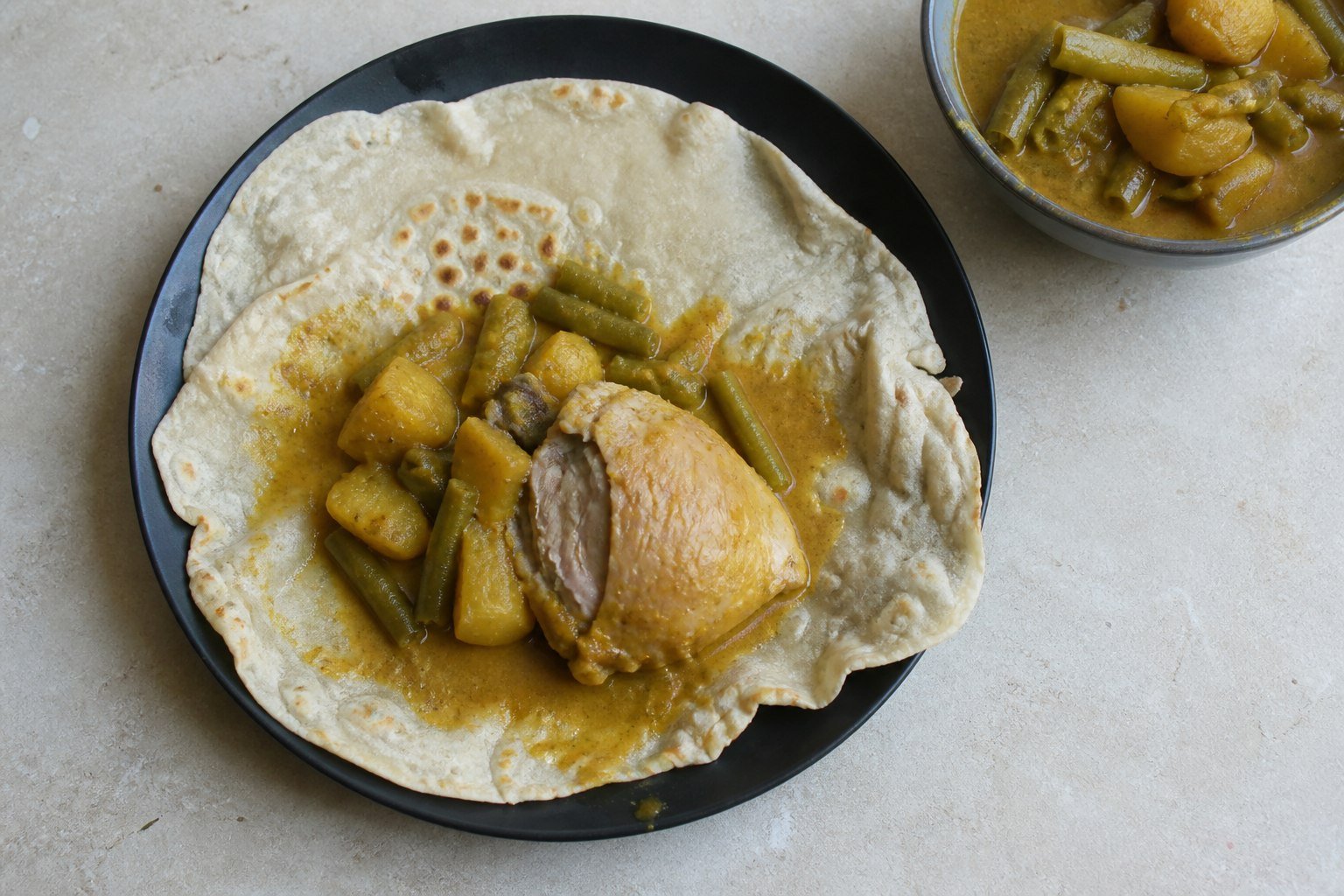 An open Surinamese roti topped with skinless masala chicken, potatoes, long beans, and gravy.