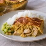 Surinamese pom casserole with chicken served beside rice and cucumber relish.