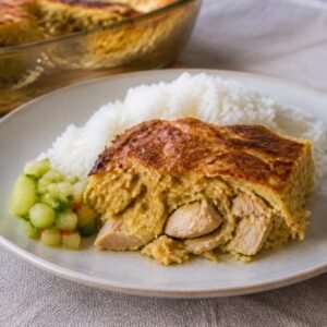 Surinamese pom casserole with chicken served beside rice and cucumber relish.