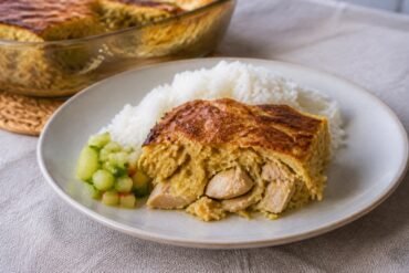 Surinamese pom casserole with chicken served beside rice and cucumber relish.