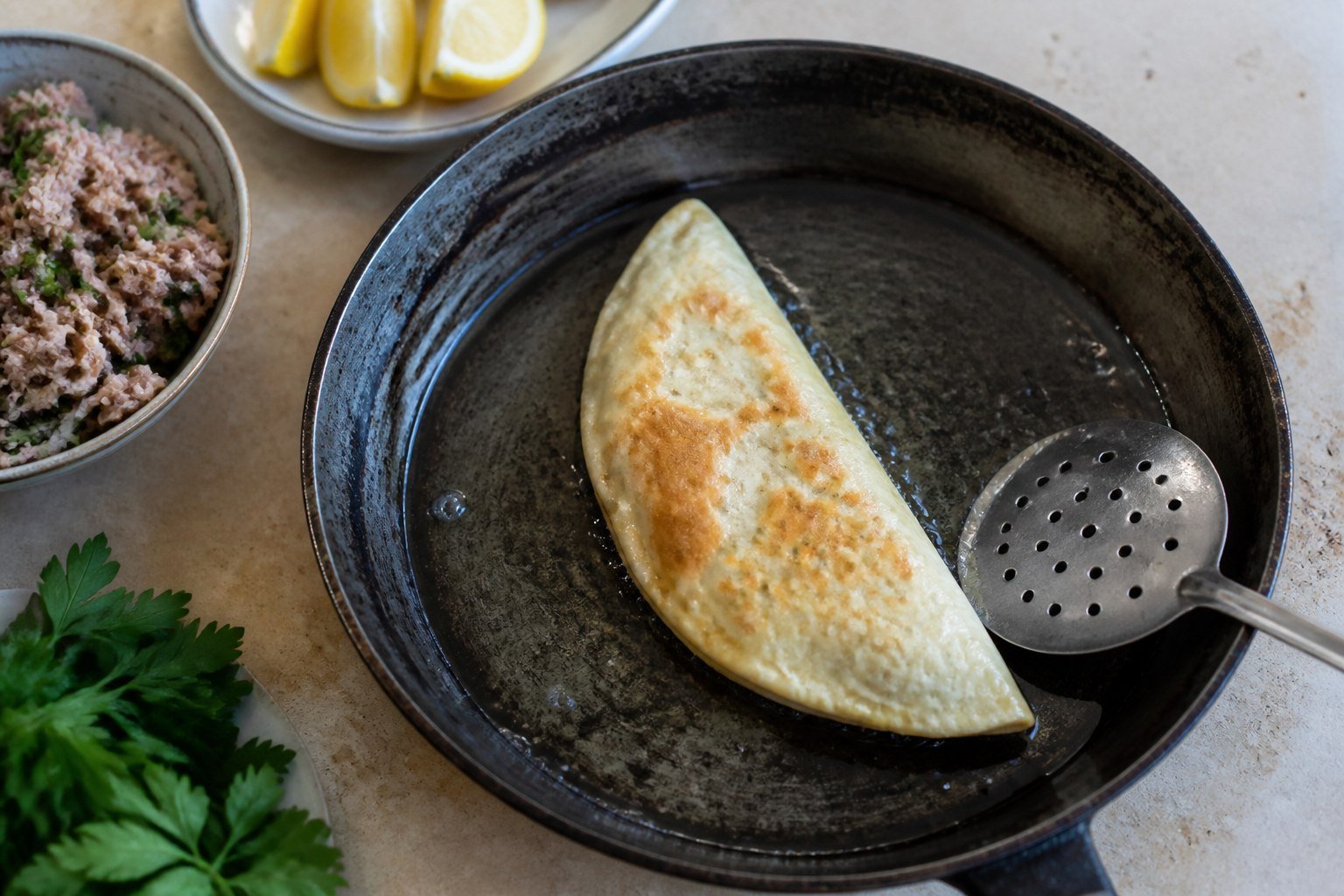 A Tunisian brik pastry frying in a shallow skillet with tuna filling nearby.