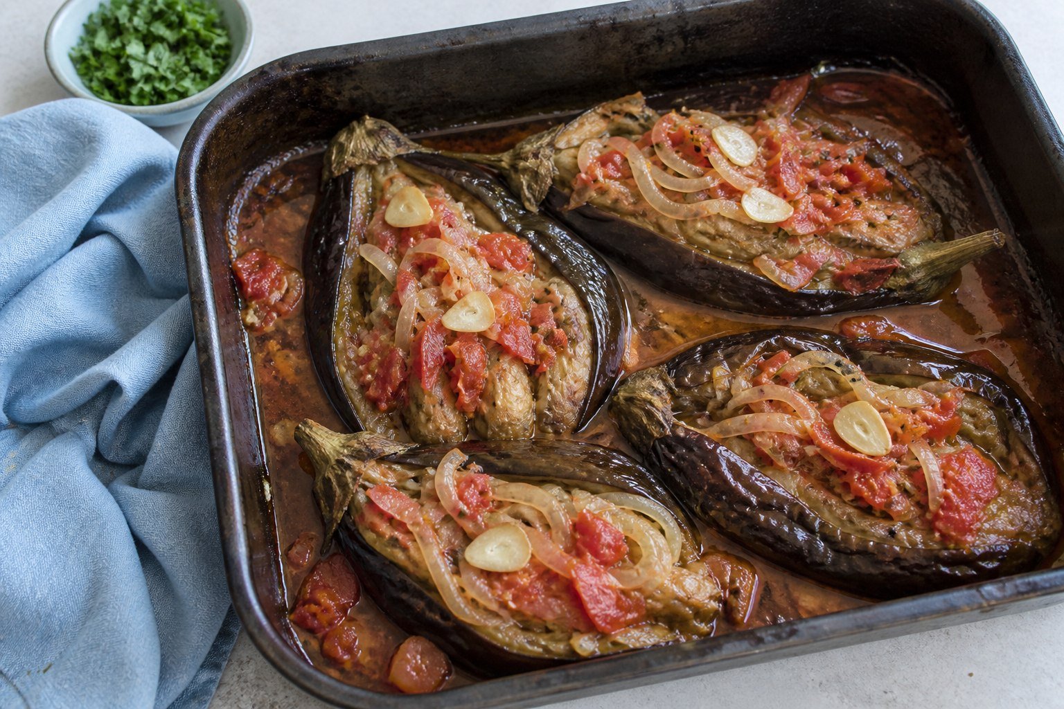 Imam bayildi eggplants baked with sliced onion, tomato, garlic, and olive oil in a roasting pan.