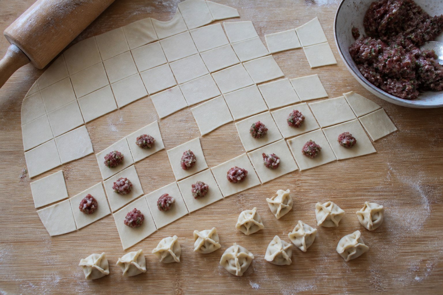 Small Turkish manti dumplings being filled and folded on a wooden board.