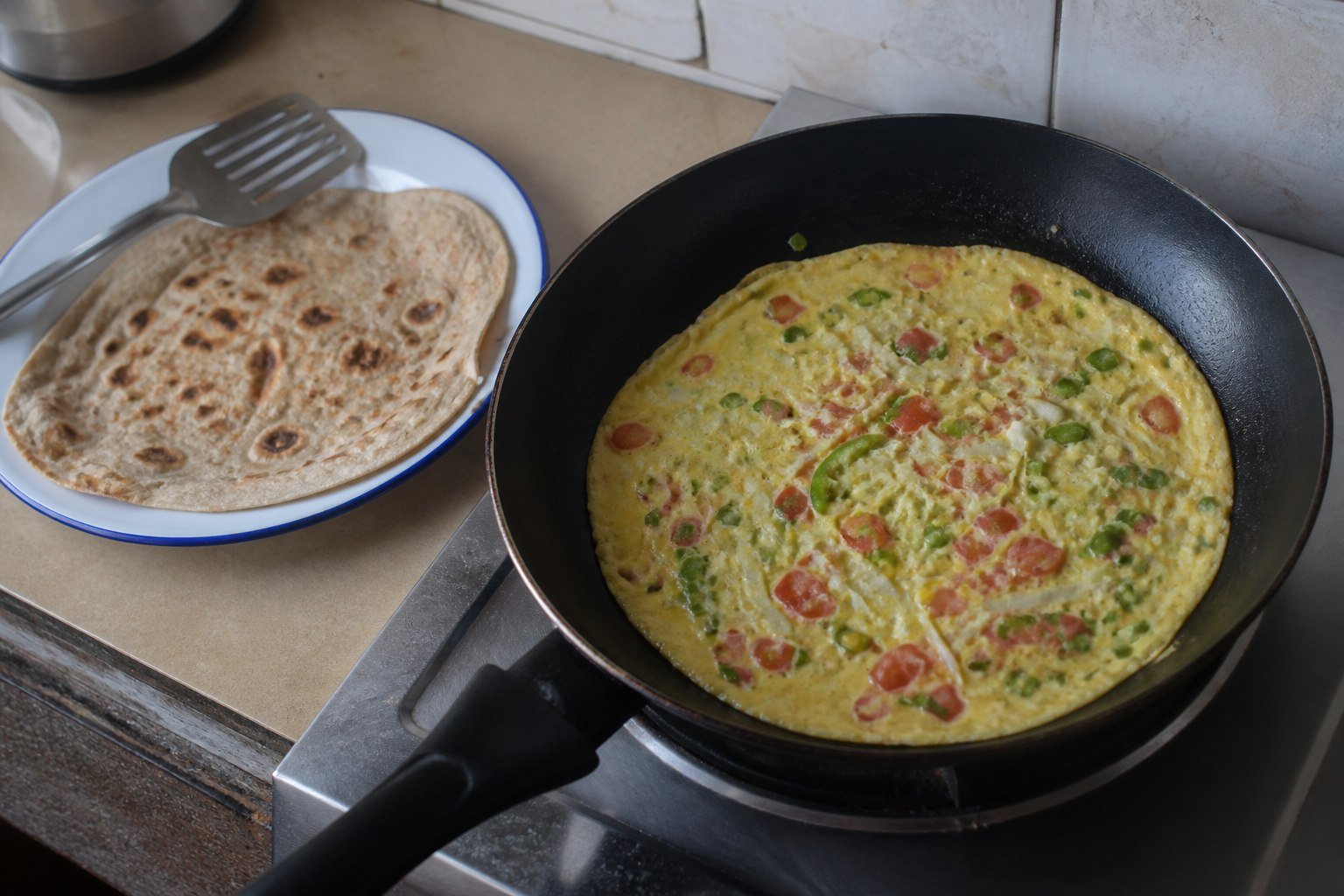 A thin vegetable omelet cooking beside a fresh chapati for Ugandan rolex.