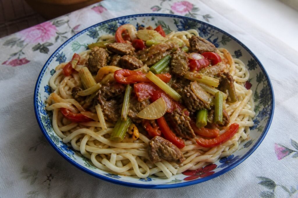 Uyghur lagman hand-pulled noodles topped with lamb, tomato, peppers, onion, and celery.
