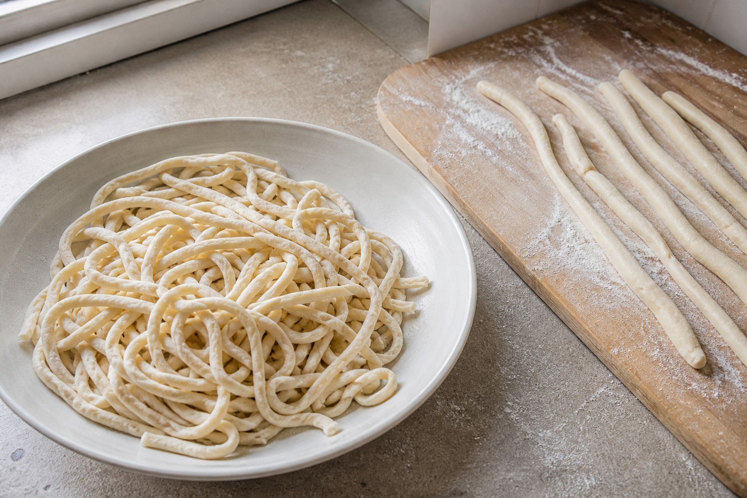 Irregular handmade lagman noodles and dough ropes resting on a floured kitchen work surface.