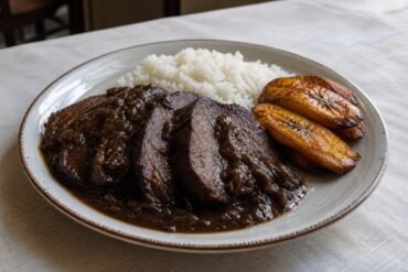 Venezuelan asado negro sliced in dark onion sauce with white rice and fried plantain.