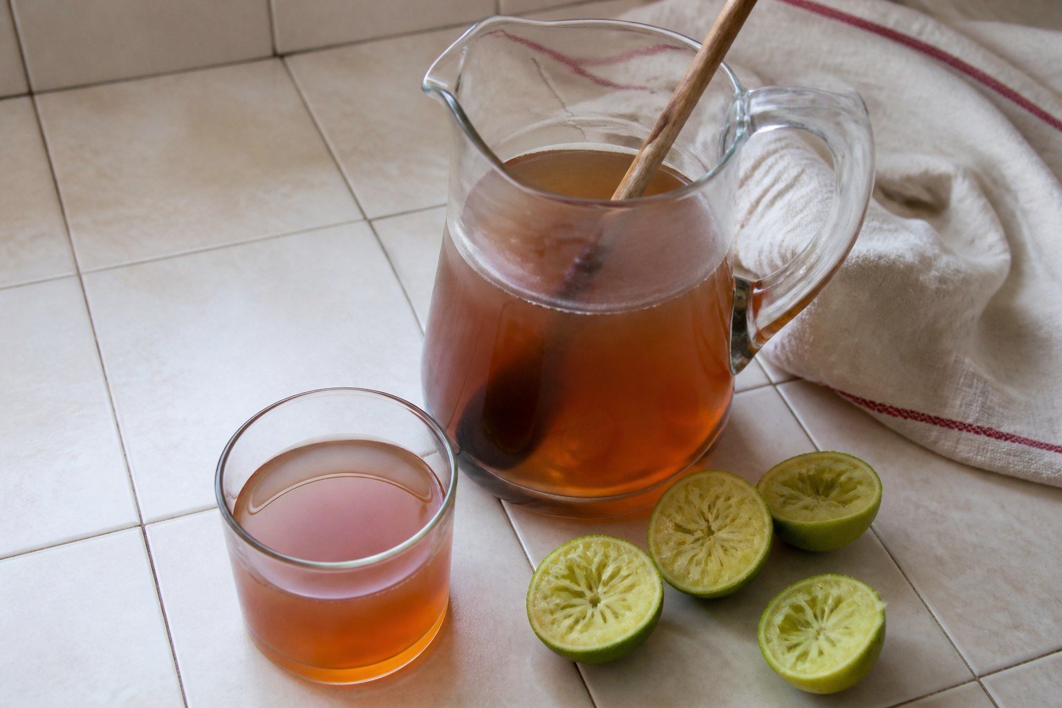 Papelon con limon being mixed in a clear pitcher beside freshly squeezed lime halves.