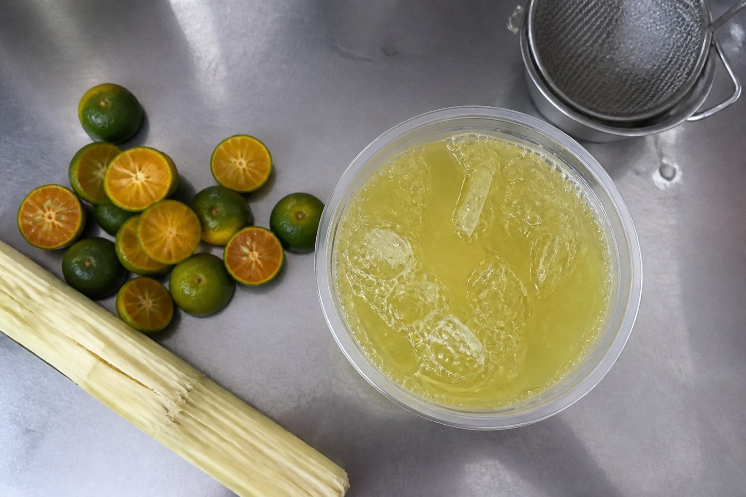 Vietnamese sugarcane juice with ice in a clear street cup beside fresh kumquats and cane.