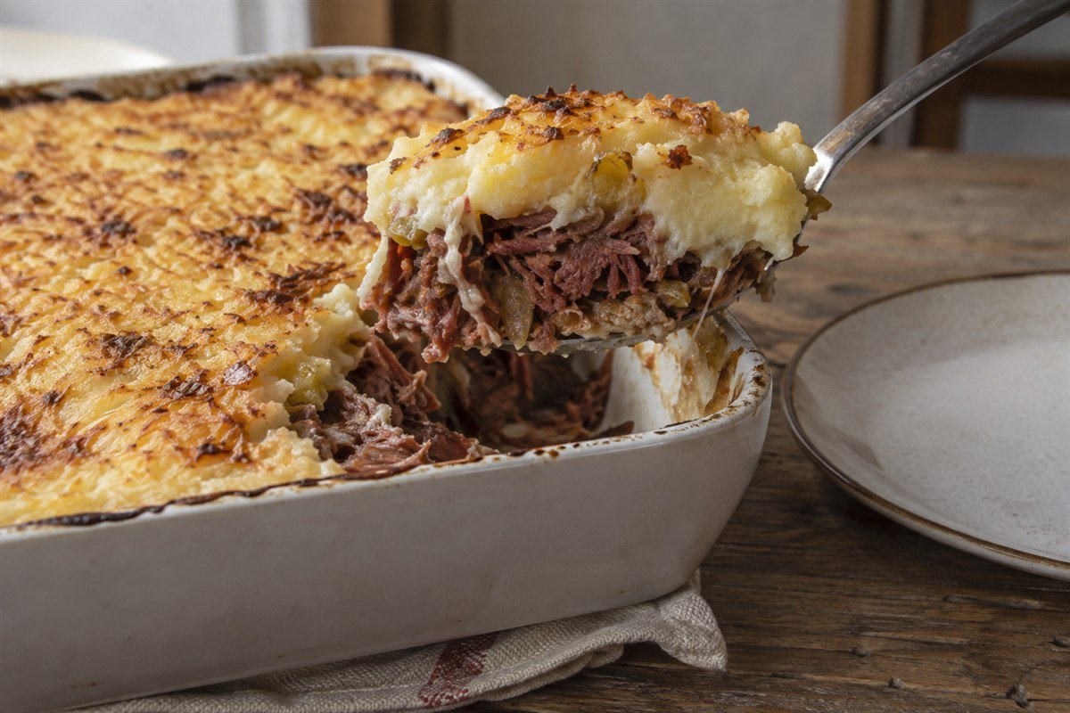 A serving spoon lifting cassava mash and shredded carne seca from a Brazilian casserole.