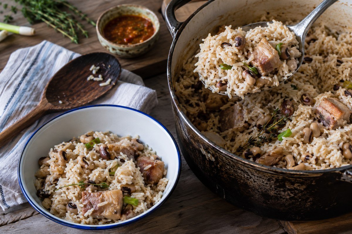 Guyanese Cook-Up Rice being served from a heavy pot with black-eyed peas and pork.