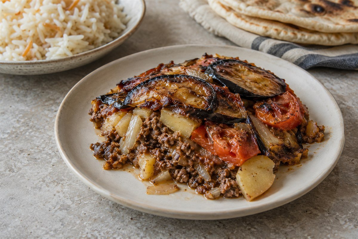 A serving of Iraqi Tepsi Baytinijan with layered eggplant, beef, potatoes, and tomatoes.