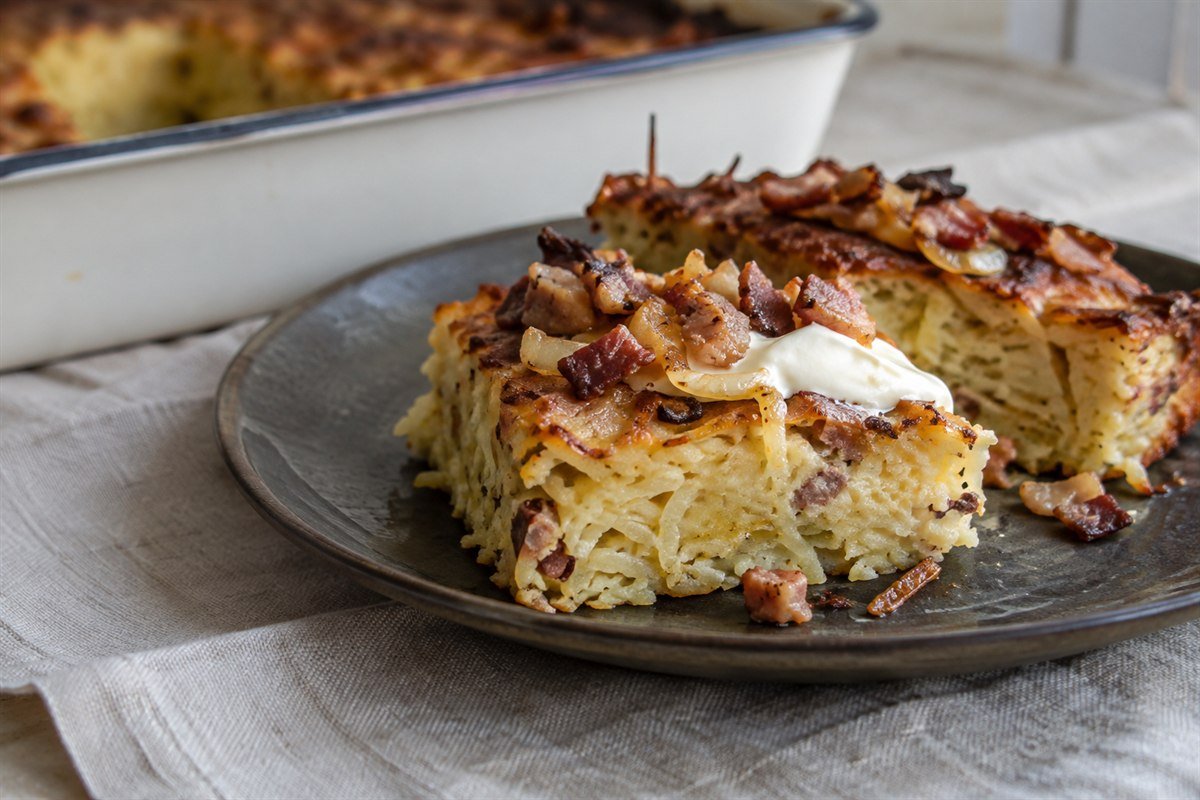 A slice of Lithuanian Kugelis topped with sour cream, bacon, and onions.