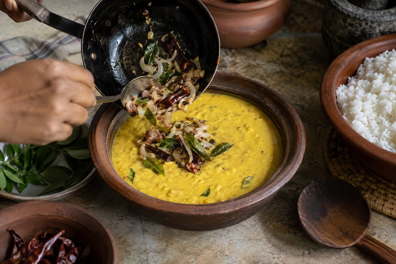 A tempering of onion, mustard seeds, dried chili, and curry leaves being spooned over Sri Lankan dhal curry.