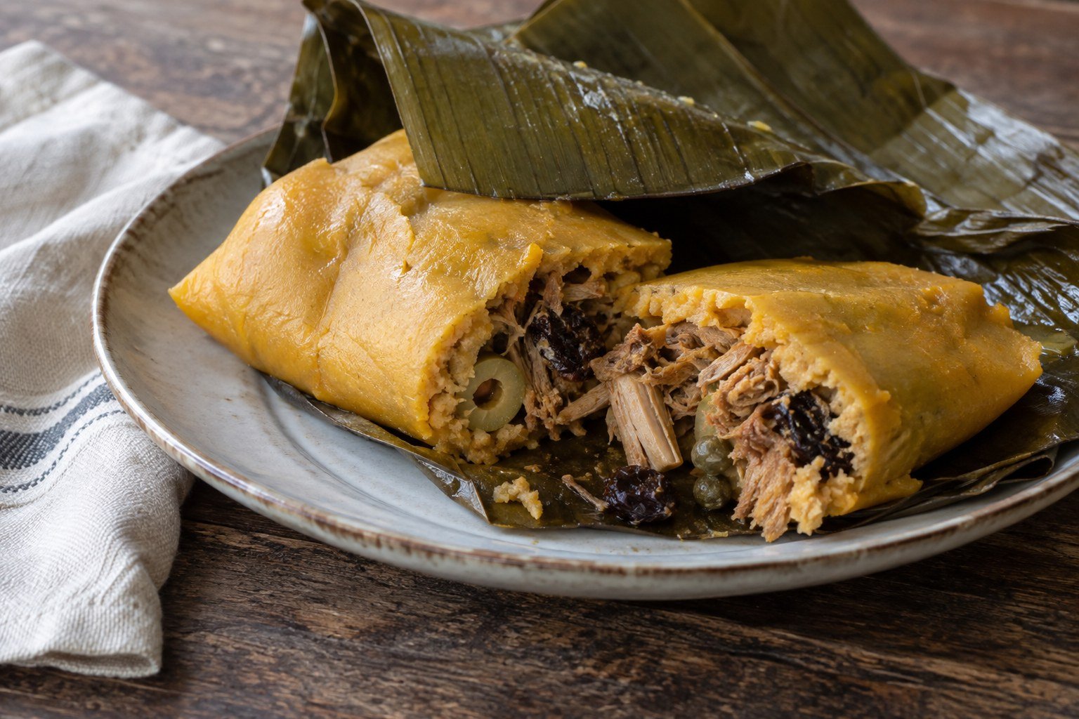 A Venezuelan hallaca opened to show its corn dough and savory meat filling.