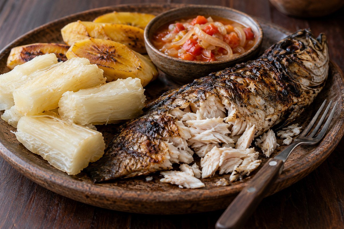 A close serving view of Angolan mufete with grilled fish flaked beside cassava and plantain, with onion-tomato sauce in a small bowl.