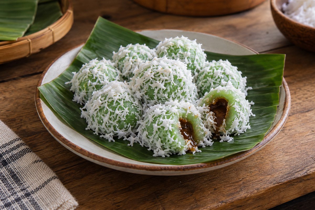 Indonesian klepon rice cakes with green pandan dough, palm sugar centers, and fresh grated coconut arranged naturally on a banana leaf-lined plate.
