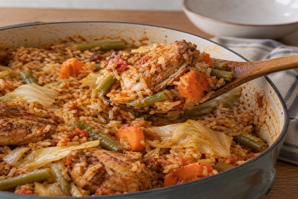 A wooden spoon serving tomato rice, chicken, and vegetables from Burkinabè riz gras.