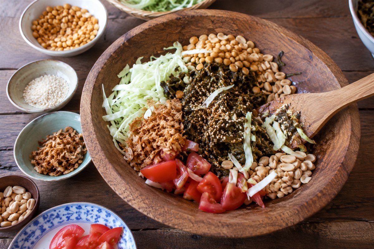 Burmese laphet thoke being mixed in a shallow bowl with crunchy toppings and lime.