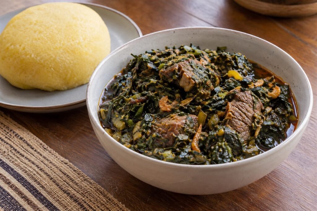 Cameroonian eru with leafy greens, beef, crayfish, red palm oil, and soft garri.