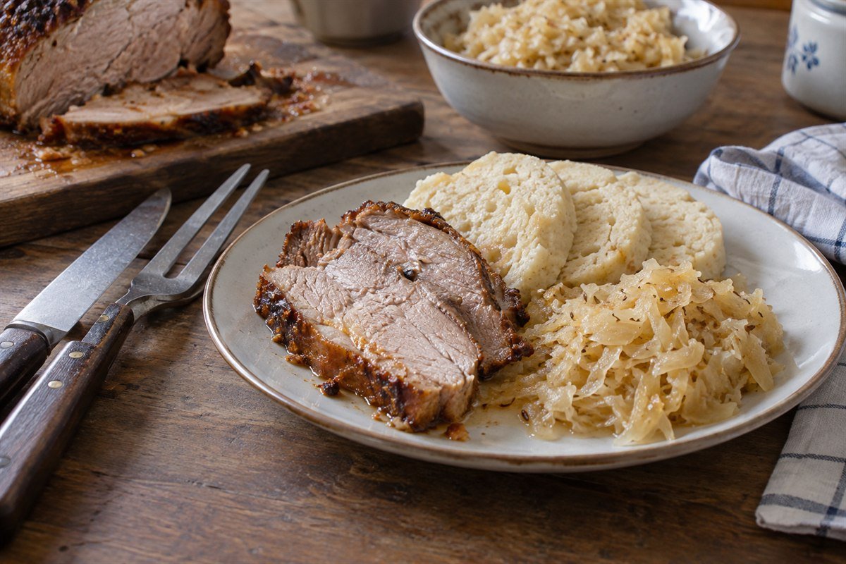 Czech roast pork with dumplings and sauerkraut being served from a home-style table.