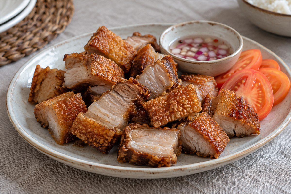Crisp Filipino lechon kawali pork belly with vinegar dip and tomatoes.