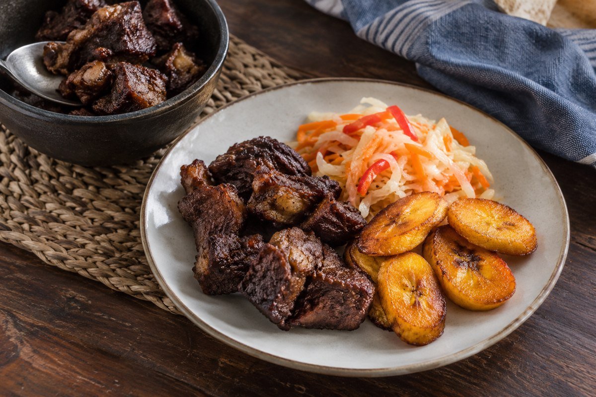 A home-style serving of Haitian Tassot with fried beef, plantains, and pikliz.