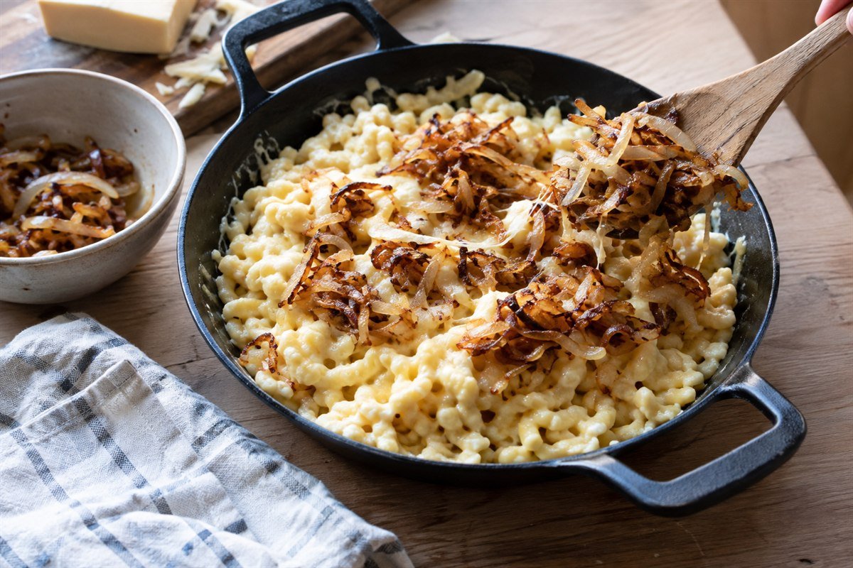 Cheese spaetzle being finished with caramelized onions in a cast-iron pan.