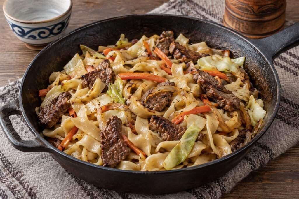 Mongolian tsuivan beef and vegetables tossed with noodles in a rustic pan.