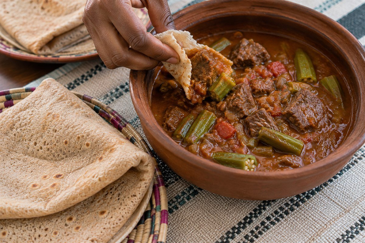 Kisra flatbread being used to scoop beef mullah stew with okra.